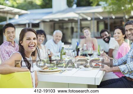 Stock Image - Friends smiling at table outdoors. Fotosearch