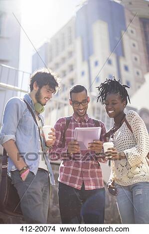 Picture - Friends using digital tablet on city street. Fotosearch
