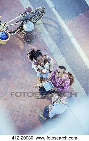 Stock Image - Friends using digital tablet on city street. Fotosearch