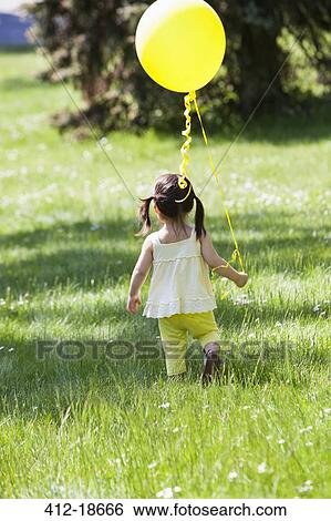 Stock Photograph - Girl carrying balloon in backyard. Fotosearch
