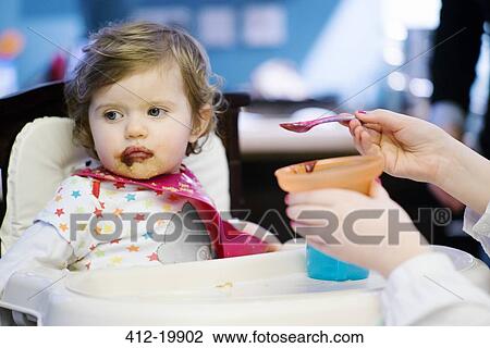 Girl feeding baby girl in high chair View Large Photo Image Stock Image - Girl feeding baby girl in high chair. Fotosearch