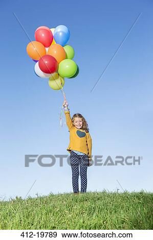 Girl holding bunch of balloons on grassy hill View Large Photo Image Stock Photo - Girl holding bunch of balloons on grassy hill. Fotosearch