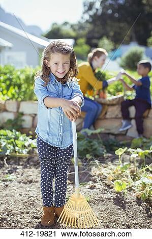 Stock Image - Girl holding rake in garden. Fotosearch