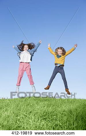 Stock Photo - Girls jumping for joy on grassy hill. Fotosearch
