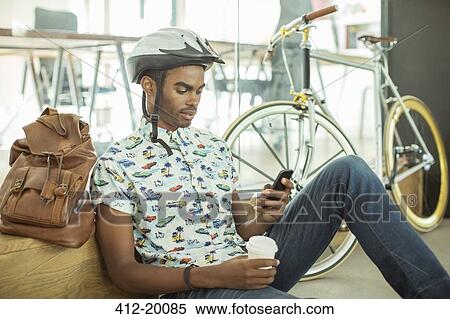 Man in bicycle helmet using cell phone in office View Large Photo Image Stock Photography - Man in bicycle helmet using cell phone in office. Fotosearch