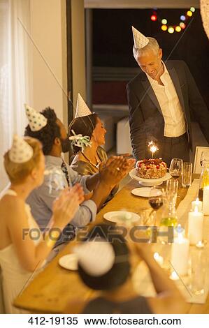 Stock Photography - Man serving birthday cake at party. Fotosearch