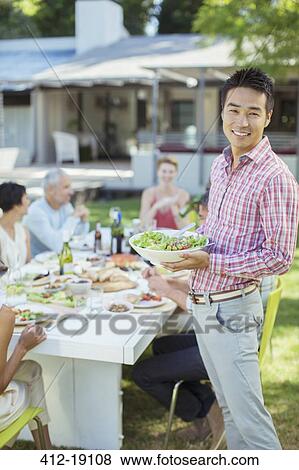 Stock Photo - Man serving friends at table outdoors. Fotosearch