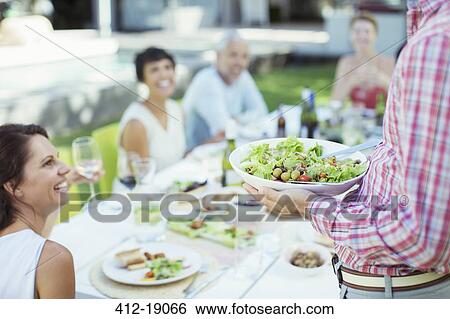 Stock Photograph - Man serving friends at table outdoors. Fotosearch