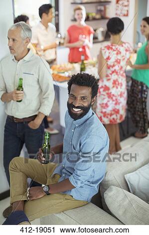 Man smiling on sofa at party View Large Photo Image Stock Image - Man smiling on sofa at party. Fotosearch