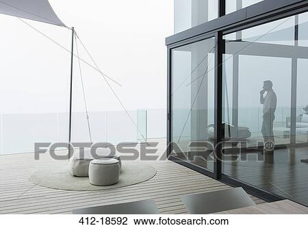 Stock Image - Man talking on cell phone in modern living room. Fotosearch