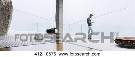 Man using cell phone on balcony of modern house View Large Photo Image Stock Photograph - Man using cell phone on balcony of modern house. Fotosearch