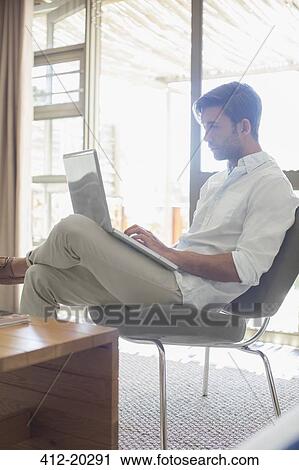 Stock Image - Man using laptop in living room. Fotosearch