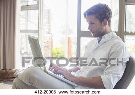 Stock Photography - Man using laptop in living room. Fotosearch