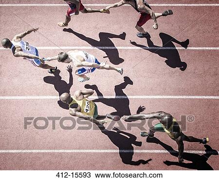 Stock Image - Relay runners handing off batons on track. Fotosearch