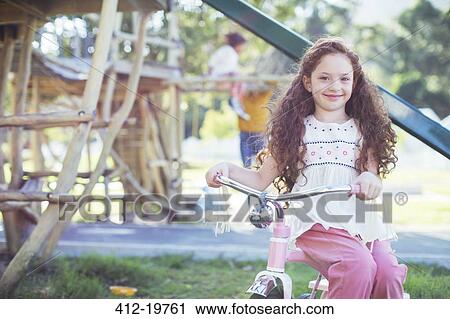 Stock Image - Smiling girl sitting on bicycle at playground. Fotosearch
