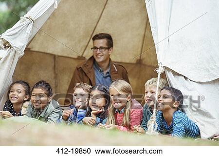 Stock Image - Students and teacher smiling in tent at campsite. Fotosearch