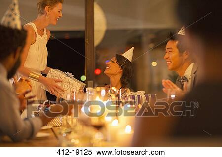 Stock Photography - Woman giving friend present at birthday party. Fotosearch