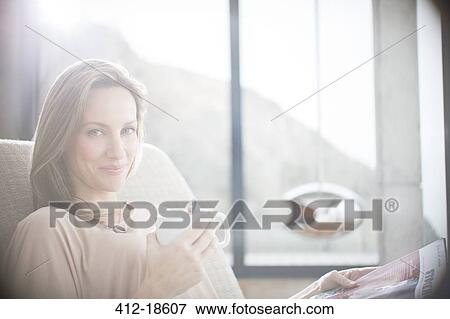 Stock Photo - Woman having cup of coffee on sofa. Fotosearch