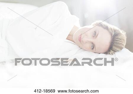 Stock Photo - Woman in bathrobe laying on bed. Fotosearch