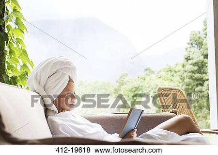 Stock Photo - Woman in bathrobe reading on sofa. Fotosearch