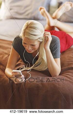 Woman listening to mp3 player on bed View Large Photo Image Stock Photo - Woman listening to mp3 player on bed. Fotosearch