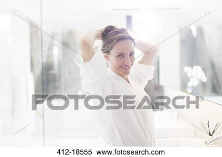 Stock Photography - Woman putting up her hair in bathroom. Fotosearch