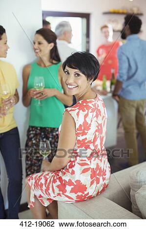 Stock Image - Woman smiling on sofa at party. Fotosearch
