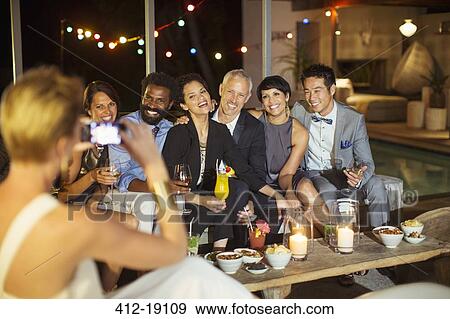 Stock Photo - Woman taking picture of friends at party. Fotosearch