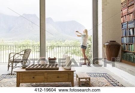 Picture - Woman taking picture of landscape from balcony. Fotosearch