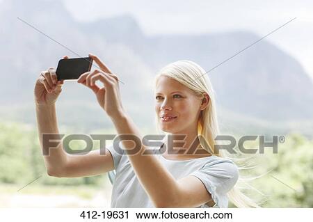 Stock Image - Woman taking pictures in rural landscape. Fotosearch