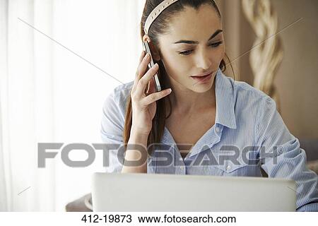 Woman talking on cell phone at laptop View Large Photo Image Stock Image - Woman talking on cell phone at laptop. Fotosearch