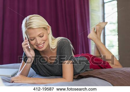 Stock Photo - Woman talking on cell phone on bed. Fotosearch