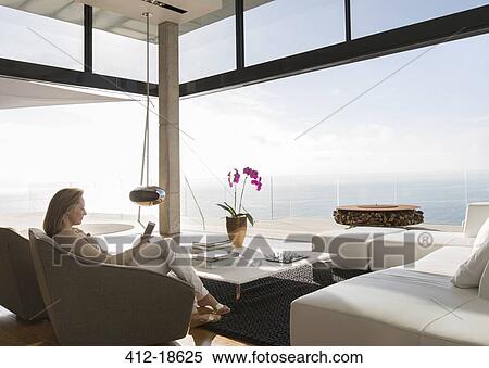 Stock Photography - Woman using cell phone in modern living room. Fotosearch