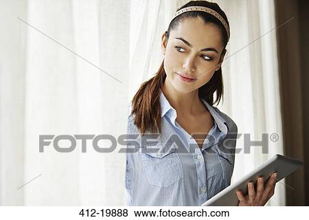 Woman using digital tablet by window View Large Photo Image Stock Photo - Woman using digital tablet by window. Fotosearch