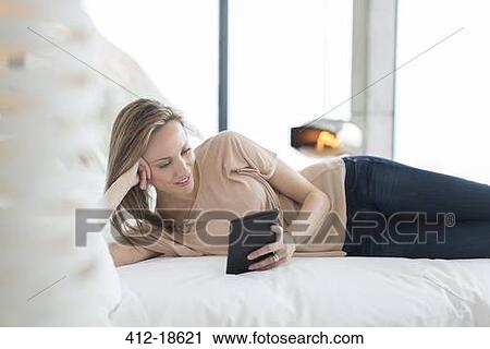 Stock Image - Woman using digital tablet on bed. Fotosearch
