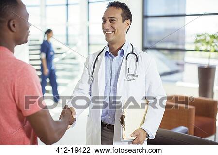 Stock Image - Doctor and patient shaking hands in hospital. Fotosearch
