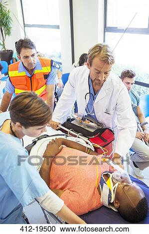 Stock Image - Doctor, nurse and paramedic wheeling patient in hospital. Fotosearch