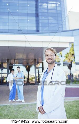 Stock Image - Doctor smiling outside hospital. Fotosearch