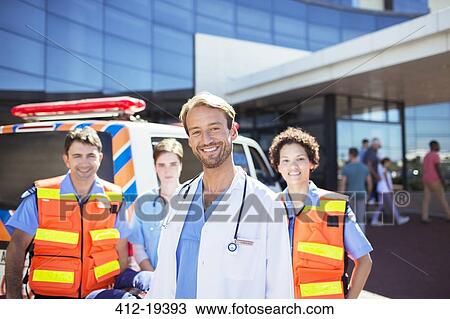 Stock Image - Doctor smiling with paramedics in hospital parking lot. Fotosearch