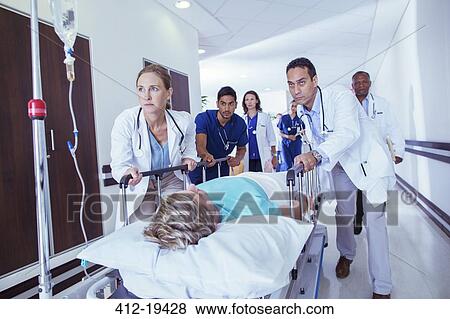 Stock Photo - Doctors and nurses wheeling patient down hospital hallway. Fotosearch