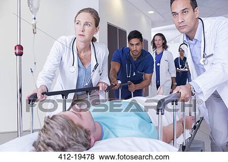 Stock Photo - Doctors wheeling patient in hospital hallway. Fotosearch