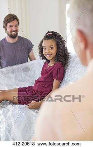 Stock Photo - Family lifting couch with young girl sitting on top. Fotosearch