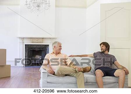 Stock Photograph - Father and son sitting on couch in living space. Fotosearch