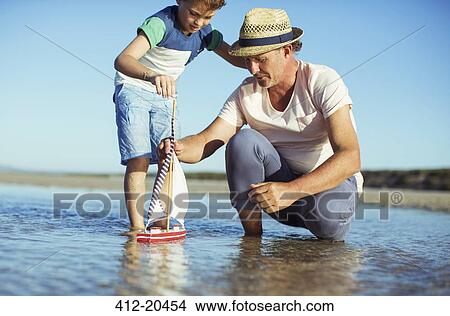 Grandfather and grandson playing with toy boat in water View Large Photo Image Picture - Grandfather and grandson playing with toy boat in water. Fotosearch