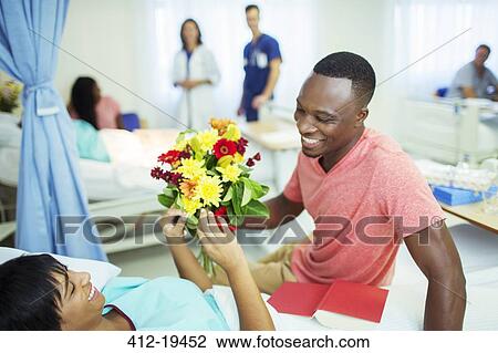 Man giving girlfriend bouquet of flowers in hospital View Large Photo Image Stock Image - Man giving girlfriend bouquet of flowers in hospital. Fotosearch