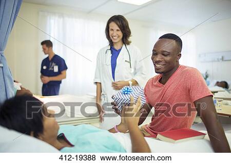 Stock Photo - Man giving girlfriend present in hospital. Fotosearch