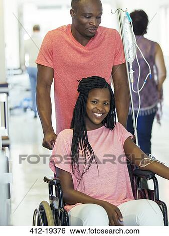 Stock Photograph - Man wheeling girlfriend in hospital hallway. Fotosearch