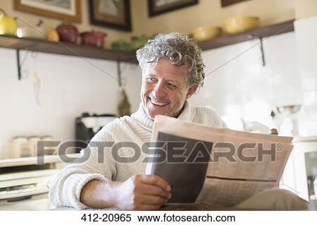 Stock Photography - Older man reading news paper in kitchen. Fotosearch