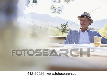 Stock Photograph - Older man sitting at outdoor dinning table . Fotosearch