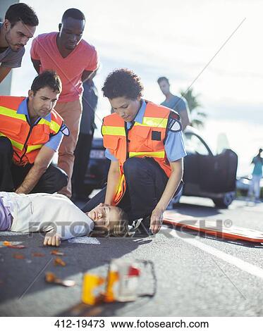 Stock Image - Paramedics examining injured girl on street. Fotosearch
